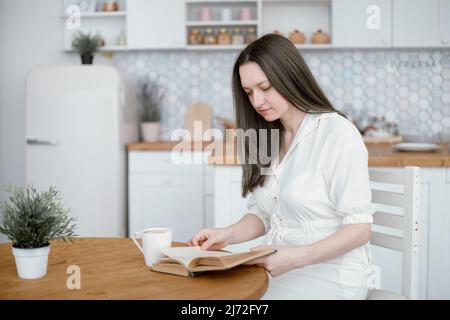 giovane donna che legge un libro seduto al tavolo da cucina . Foto Stock