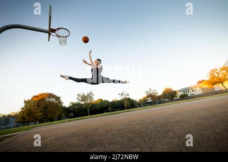 Ballerino balletto a mezz'aria che gioca a basket su un campo all'aperto Foto Stock