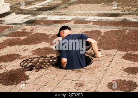 Un lavoratore si arrampica fuori da un tombino aperto nella strada. Pericoloso botola aperta non protetta sulla strada. Incidente con una botola fognaria in città. Il con Foto Stock