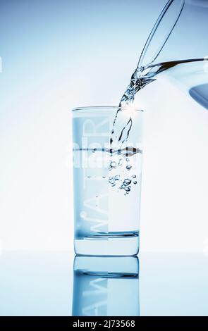 L'acqua viene versata dalla caraffa di vetro al vetro alto Foto Stock