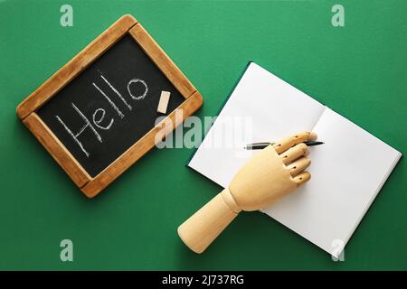 Gesso bordo con parola CIAO, mano di legno, penna e notebook su sfondo verde Foto Stock