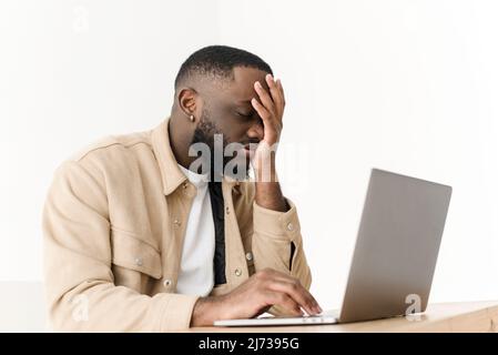 Il giovane uomo nero ha lavorato in modo eccessivo, soffrendo di mal di testa mentre si siede al portatile a casa Foto Stock