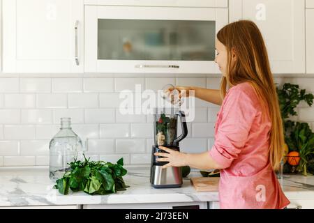 Femmina sorridente, versa l'acqua in un frullato verde. Donna sana food.Happy su dieta detox, frutta tritata in mixer . Foto Stock