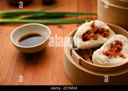 Immagine ravvicinata, gustoso panino cinese per barbecue o panna di maiale al vapore in un vaporetto di bambù servito con salsa di soia. Foto Stock