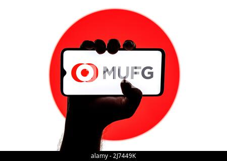 Smartphone con logo Mitsubishi UFJ Financial Group sullo schermo in mano applaiata sullo sfondo della bandiera giapponese Foto Stock