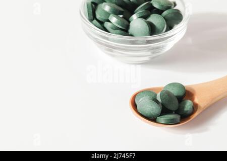 additivi naturali e superfood. pillole di alghe spirulina verde in cucchiaio e ciotola di vetro su sfondo bianco. spazio sano concept.organic copie di cibo Foto Stock