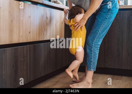 La madre alza il bambino, che grida che vuole fra le braccia della madre. Prendi il bambino in piedi. Cura della famiglia. Cura del bambino. Foto Stock