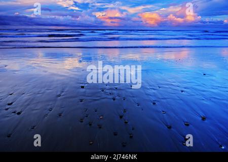 La spiaggia di ciottoli e sabbia all'alba, con le onde blu scuro e le nuvole d'arancio, Costa Rica Foto Stock