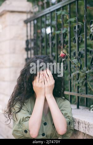 Donna che nasconde il volto con le mani all'aperto Foto Stock