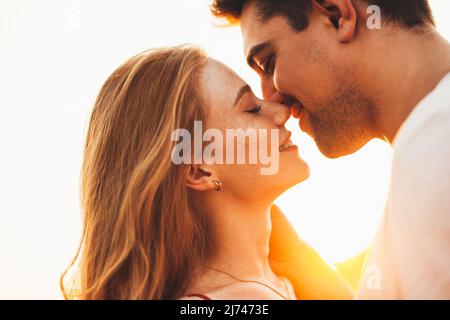 Primo piano ritratto di una donna e di un uomo che chiudono gli occhi e che vogliono baciare con il sole che splende dietro di loro. Vista laterale. Primo piano verticale. Foto Stock