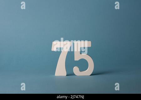 Numero settantacinque in legno bianco 75 su sfondo blu. Foto Stock