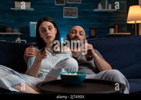 Uomo che guarda film e donna che cambia canale, facendo la selezione di film in televisione. Ragazza che usa il controllo del rmeote TV e ragazzo che beve birra dalla bottiglia. POV Foto Stock