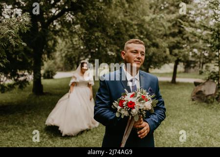 Il giovane uomo biondo caucasico europeo sposa in abito blu e donna dai capelli neri sposa in abito da sposa bianco con velo lungo e tiara sulla testa. Prima Foto Stock