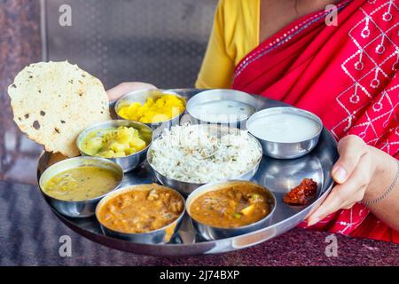 Bella donna brunetta in rosso sari mangiare con appetito tradizionale thali wirh aumento, curd, dal ristorante Goa masala tè Foto Stock