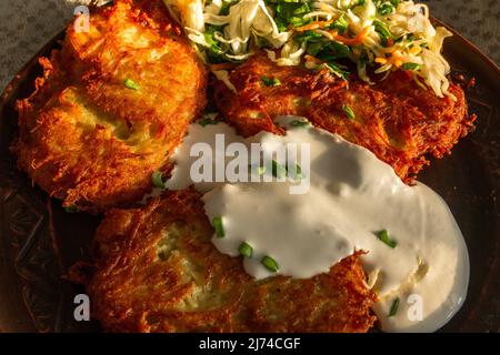 Frittelle di patate fritte su un piatto marrone di lino, panna acida, cipolle verdi, coleslaw e carote. Cibo, frittelle di patate, piatto Foto Stock