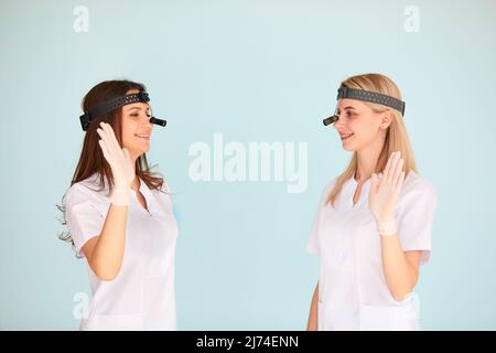 Due otolaringologi femminili sono contenti del lavoro che hanno fatto e stringono le mani su uno sfondo chiaro. Concetto di protezione della salute Foto Stock
