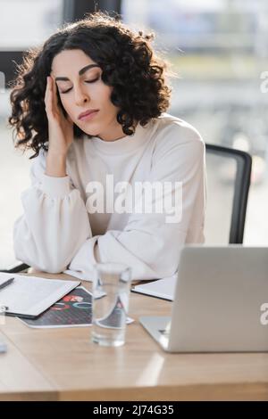 Donna d'affari araba stanca seduto vicino agli appunti e al computer portatile in ufficio Foto Stock