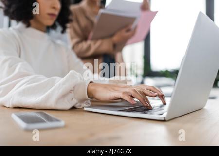 Vista ritagliata di una donna d'affari musulmana che usa un laptop vicino a un collega offuscato in ufficio Foto Stock