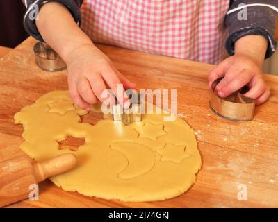 la foto mostra una giovane ragazza (mano) che usa la taglierina per biscotti per preparare i biscotti di natale fatti in casa Foto Stock