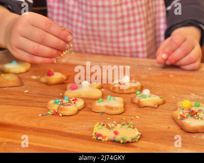 la foto mostra una mano dei bambini che decorano biscotti al burro con spolverini Foto Stock