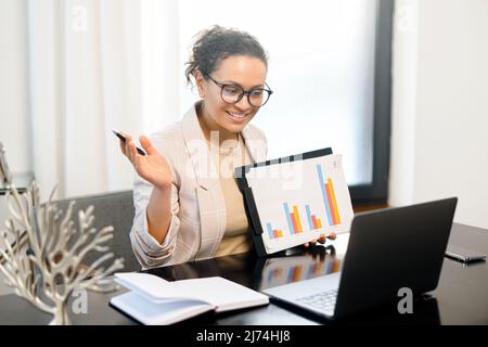 Dipendente di mezza età durante una riunione virtuale, che mostra i grafici nella webcam del laptop, donna d'affari coinvolto conferenza, tutor o business coach leader webinar Foto Stock