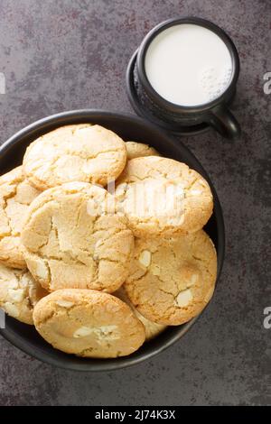 Biscotti frollini con noci di macadamia e cioccolato bianco con una tazza di latte da vicino. Vista dall'alto verticale Foto Stock