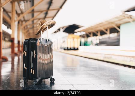 Concetto di viaggio estivo. Bagaglio con cappello di paglia sulla stazione ferroviaria vicino alla ferrovia. Foto Stock