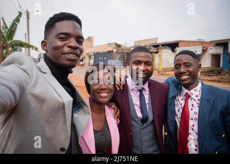 Un gruppo di amici prende insieme un selfie, giovani adulti africani ben vestiti nel centro della città, Sapiologie africane Foto Stock