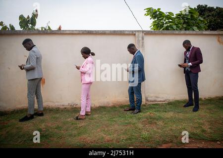 Un gruppo di giovani africani ben vestiti usa i loro smartphone in linea mantenendo una distanza di sicurezza durante la pandemia Foto Stock