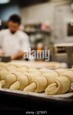 croissant seduti su una padella in attesa di essere messi in forno con un panettiere che lavora sullo sfondo Foto Stock