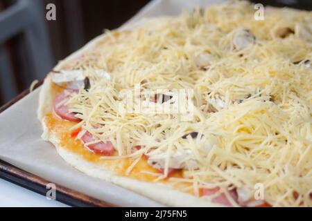 Defocalizzare in primo piano la pizza intera con mozzarella grattugiata. Defocalizzare gli ingredienti sfocati per la pizza sull'impasto. Spazio di copia. Cucina italiana b Foto Stock