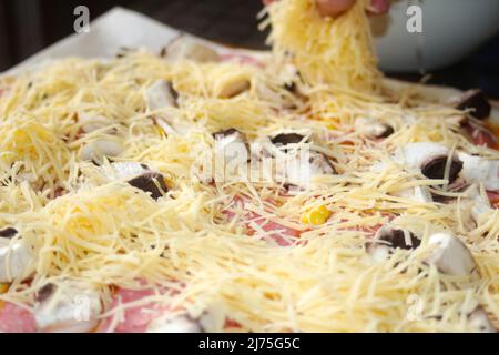 Defocalizzare il primo piano attorno alla pizza intera con mozzarella grattugiata sul tetto. Defocalizzare gli ingredienti sfocati per la pizza sull'impasto. Spazio di copia. Italiano Foto Stock