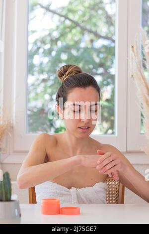 Donna con hairsyle di bun che applica mano-crema idratante su dopo la doccia sulla sua vanità a casa Foto Stock