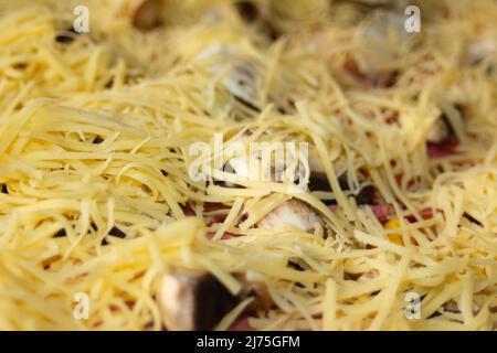 Defocalizzare il primo piano attorno alla pizza intera con mozzarella grattugiata sul tetto. Defocalizzare gli ingredienti sfocati per la pizza sull'impasto. Giallo fatto in casa Foto Stock