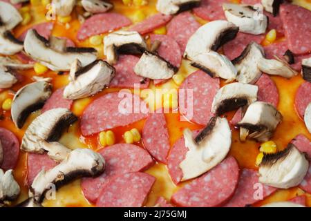 Defocalizzare gli ingredienti del primo piano per la pizza sull'impasto. Salsa di pomodoro rosso, salsicce, mais dolce. Pizza italiana fatta in casa. Base di Margarita. Home culinario. Superiore Foto Stock