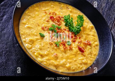 primo piano della zuppa di mais con pancetta fritta croccante sbriciolata in una ciotola nera su un tavolo di legno scuro Foto Stock