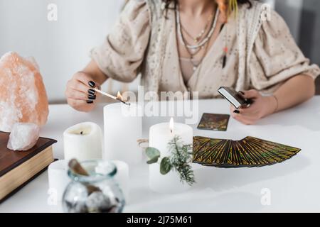 KYIV, UCRAINA - 23 FEBBRAIO 2022: Vista ritagliata del venditore di fortuna che brucia candela vicino ai cristalli e tarocchi sul tavolo Foto Stock