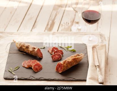Salame; parzialmente affettato su ardesia; bicchiere di vino rosso Foto Stock