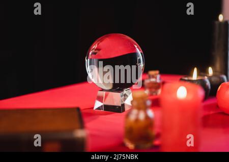Orb di vetro vicino a candele sfocate e witchcraft approvvigionamenti sul tavolo isolato su nero Foto Stock