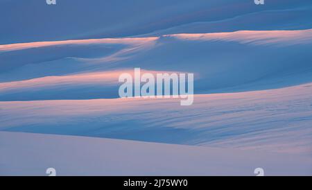 Copertura di neve ondulata illuminata arancione dalla luce soffusa del sole che tramonta. Alpi Lechtal, Austria Foto Stock