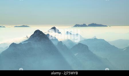 Le montagne si alzano dalla foschia in una soleggiata giornata invernale. Vista da Widderstein a Hochkünzelspitze e Zitterklapfen. In background Churfirsten e Alpstein con Säntis. Vorarlberg, Austria, Svizzera, Europa Foto Stock