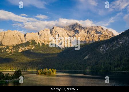 L'Eibsee e le Zugspitze nelle Alpi Bavaresi illuminate dal sole serale, in primo piano il lago con le sue acque limpide e le isole. Foto Stock