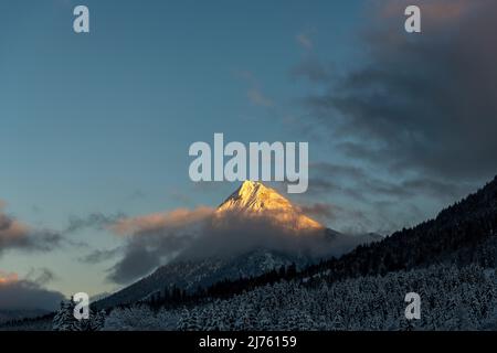 Il Guffert nei monti Rofan, mentre neve in inverno nella luce ultima sera. Alpenglow illumina solo la cima e alcune nuvole. Foto Stock