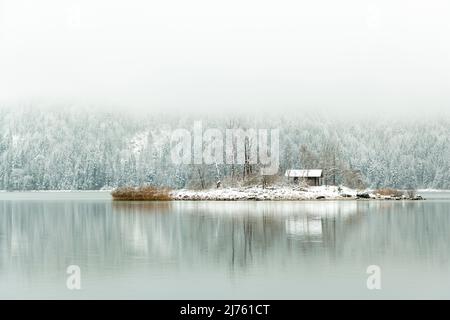 La piccola isola con capanna nell'Eibsee con neve e nuvole profonde, con una piccola capanna di legno Foto Stock