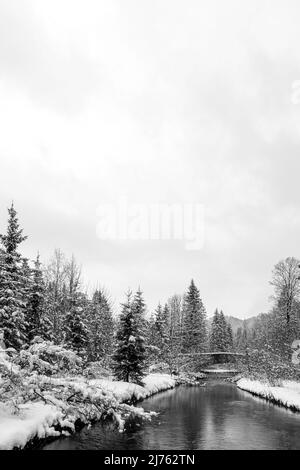 Vecchio ponte in pietra sull'Obernach tra Wallgau e Walchensee in inverno con neve fitta e nuvole. Il piccolo torrente si snoda attraverso il paesaggio invernale Foto Stock