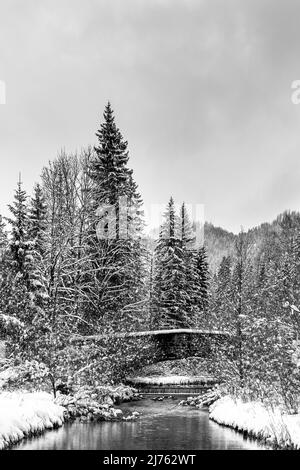 Vecchio ponte in pietra sull'Obernach tra Wallgau e Walchensee in inverno con neve fitta e nuvole. Il piccolo torrente si snoda attraverso il paesaggio invernale Foto Stock