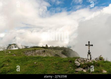 La piccola cima in metallo attraversa il Vorderskopf nel Karwendel, sullo sfondo dense nuvole e un po' di cielo blu. Foto Stock