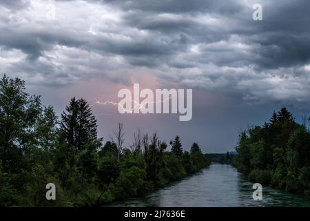 Lampi nel cielo sopra il Loisach, un noto fiume bavarese vicino a Kochel am See, tra gli altri luoghi. Le nuvole spesse e il corso del fiume, selvaggiamente soprastato, contribuiscono all'atmosfera cupa. Foto Stock