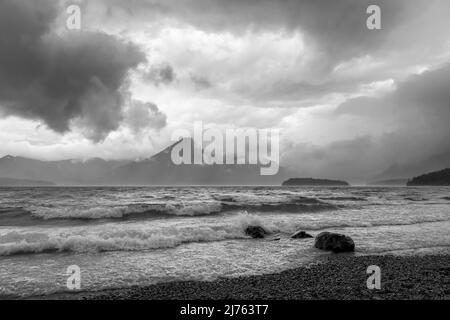 Una forte tempesta di onde, vento e nuvole sulle rive del Walchensee nelle Alpi bavaresi. Sullo sfondo la piccola isola di Sassau e l'Herzogstand tra le nuvole. Foto Stock