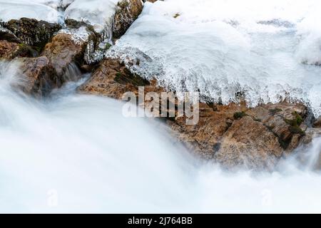L'acqua veloce del Rissbach forma lo spruzzo e la corrente. Strutture di ghiaccio e rocce formate sulla riva del torrente di montagna, delimitano l'immagine. Preso in inverno in Tirolo, Austria nella Eng, vicino al Ahornboden. Foto Stock